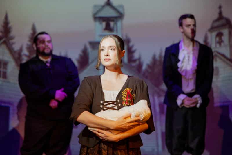 Production Photo: The character of Hester Prynne holds her baby in the foreground